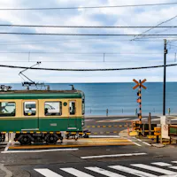 The Enoden line runs along the Shonan coast past the railroad crossing made famous by Slam Dunk. A green and cream Enoden train passing a railroad crossing with the ocean behind it on the Kamakura coast