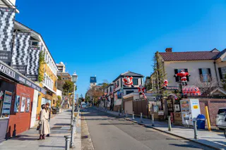 A sunny street scene in a Japanese city features a clear blue sky, people walking on the sidewalk, and buildings decorated with large Santa Claus figures for Christmas.
