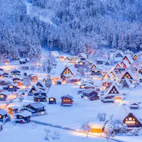 Shirakawa-go in Gifu holds its winter light-up on four January evenings in 2027. Snow-covered thatched farmhouses of Shirakawa-go lit up at dusk, with forested mountains behind the village