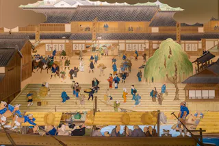 A detailed Japanese ukiyo-e style painting shows a bustling riverside market with people trading goods, boats on water, and traditional wooden buildings in the background. A willow tree stands near the stone steps.