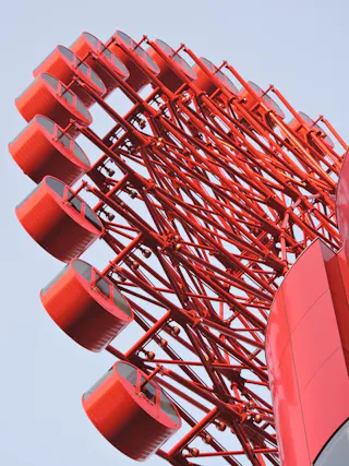 Close-up of a modern red metal structure with multiple circular platforms, set against a clear blue sky. The geometric design features intersecting beams and a glossy finish.