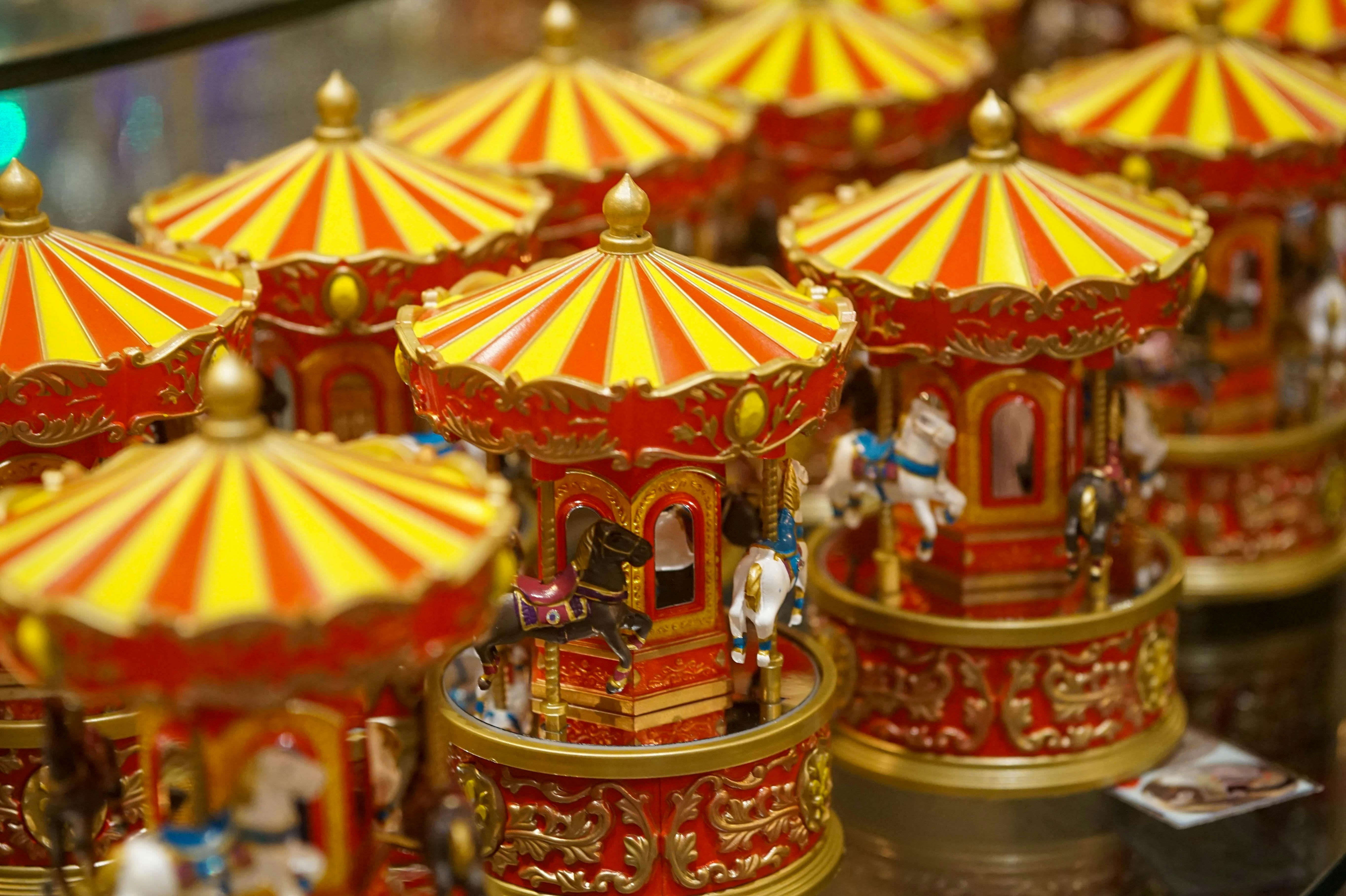Several colorful miniature carousel toys with yellow and red striped roofs, gold accents, and small painted horses are displayed closely together on a reflective surface.