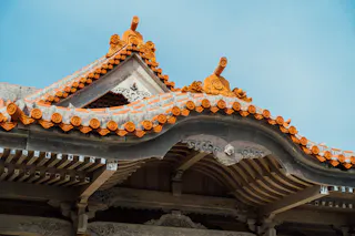 Close-up of a traditional East Asian temple roof with ornate carvings and decorative orange tiles set against a clear blue sky.