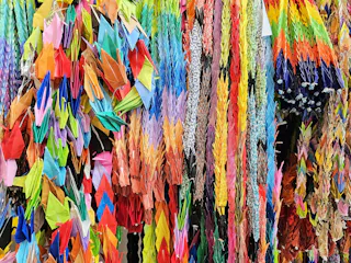 Hundreds of colorful origami paper cranes are strung together in vertical rows, creating a vibrant and intricate display of folded paper art.