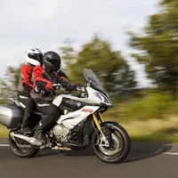 Two-up riding on a mountain road during a guided Fuji and Hakone motorcycle tour. A rider and passenger in full gear on a white adventure motorcycle leaning into a curve on a tree-lined mountain road