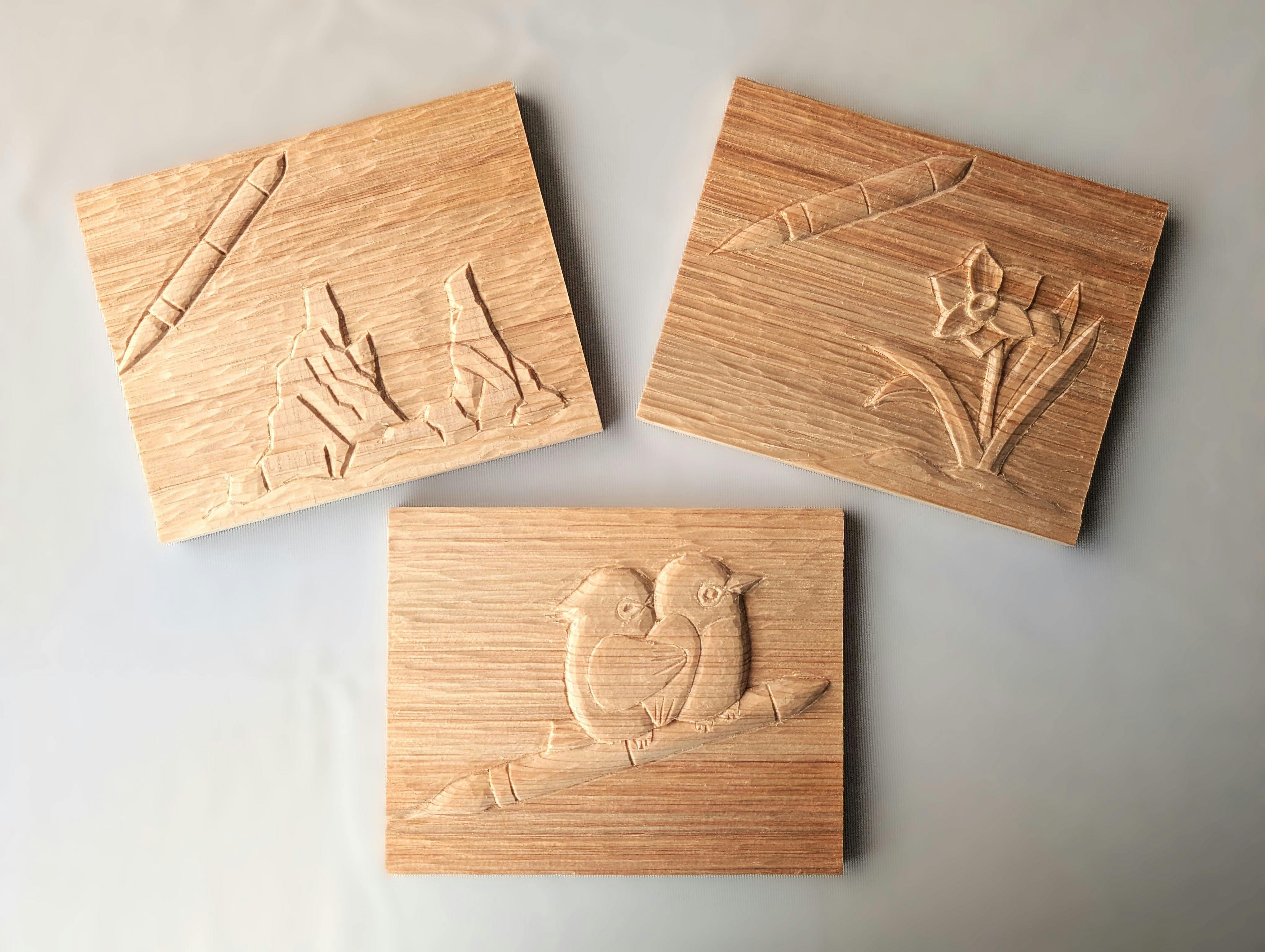 Three rectangular wooden plaques with carved designs: one shows mountains and bamboo, another depicts a bird and a flower, and the third features two birds perched on a branch. The plaques are arranged on a plain background.
