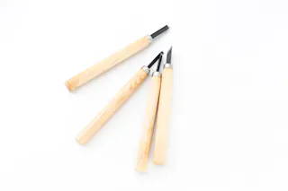 Three wood carving tools with light wooden handles and dark metal blades are arranged on a white background.