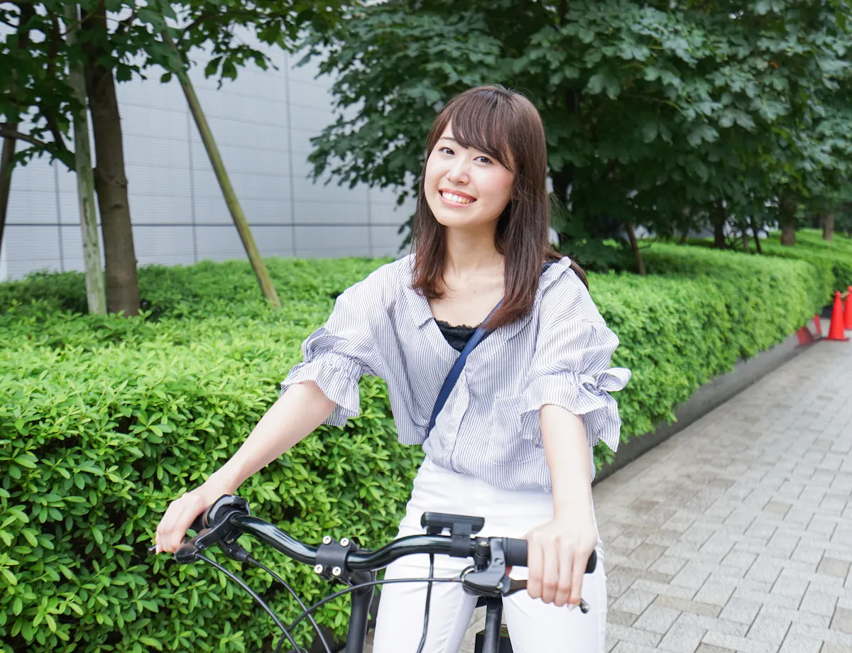 Cycling A young woman smiles while riding a bicycle on a paved path lined with green bushes and trees, with red traffic cones visible in the background.