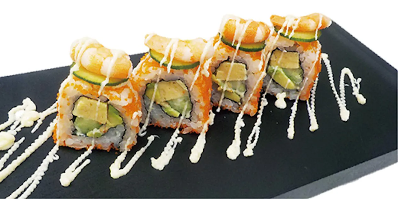 Four pieces of sushi roll topped with prawn and thin cucumber slices, drizzled with white sauce, arranged neatly on a black rectangular plate with more drizzled sauce for garnish. The sushi rolls contain avocado and other ingredients.