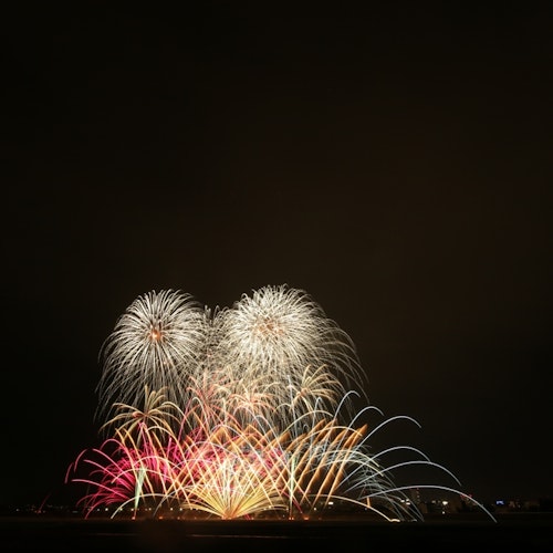 Abe River Fireworks Festival Colorful fireworks burst in the night sky above a dark landscape, creating arches and patterns of red, yellow, white, and blue light against a black background.