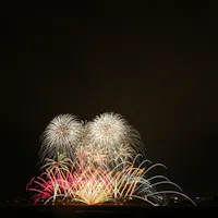 Abe River Fireworks Festival Colorful fireworks burst in the night sky above a dark landscape, creating arches and patterns of red, yellow, white, and blue light against a black background.