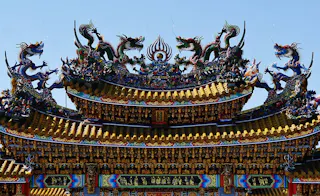 Ornate, colorful temple roof with intricate details, featuring golden tiles and large decorative dragons and phoenix sculptures against a clear blue sky.