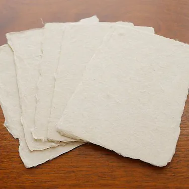Washi Papermaking Experience Five sheets of rough, handmade paper are spread out in a fan shape on a wooden surface.