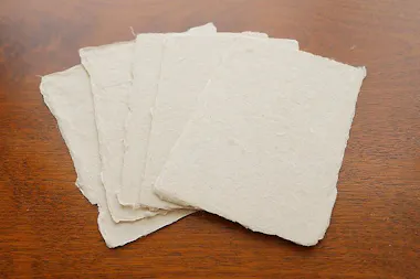 Five sheets of rough, handmade paper are spread out in a fan shape on a wooden surface.