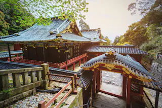 A traditional Japanese temple with ornate roofs and intricate gold details, surrounded by trees and natural scenery on a sunny day.