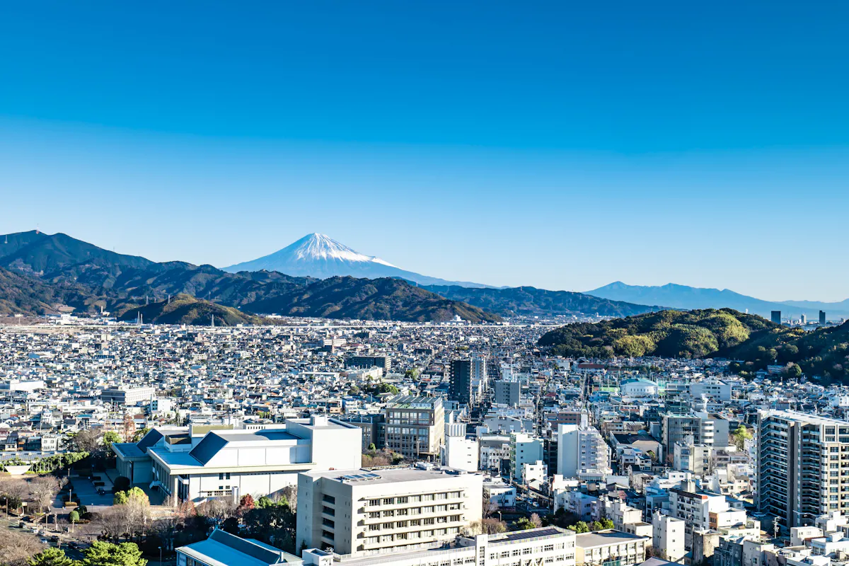Shizuoka City and Mt.Fuji A cityscape with Mount Fuji in the background under a clear blue sky. The foreground features a sprawling urban area with various buildings and greenery interspersed throughout.