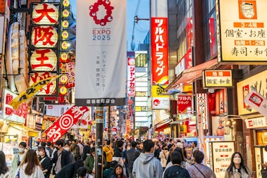 Foreground street lighting stand with expo 2025 banner, behind that many neon signs