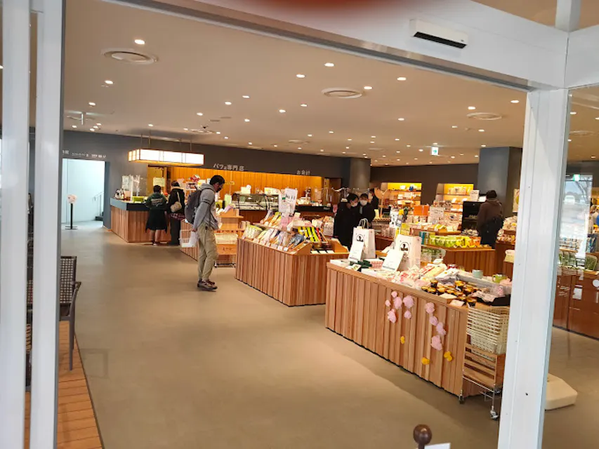 A modern grocery store interior with wooden shelves displaying various products. Customers browse near shelves with fresh produce and packaged goods. Bright lighting and neatly arranged product displays create a welcoming atmosphere.
