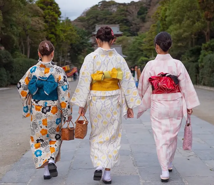 Three Japanese women in kimonos walking down a path, carrying handbags.