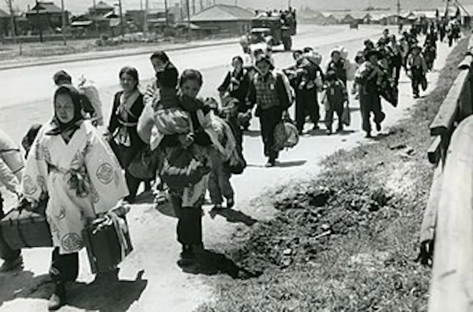 Image of people carrying luggage while walking on a road, depicting the forced relocation of Japanese settlers from Manchuria in 1946.