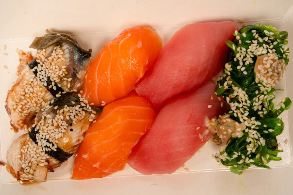 An assortment of sushi sits on a tray, featuring pieces of eel and salmon nigiri topped with sesame seeds, tuna nigiri, and a small serving of seasoned seaweed salad.