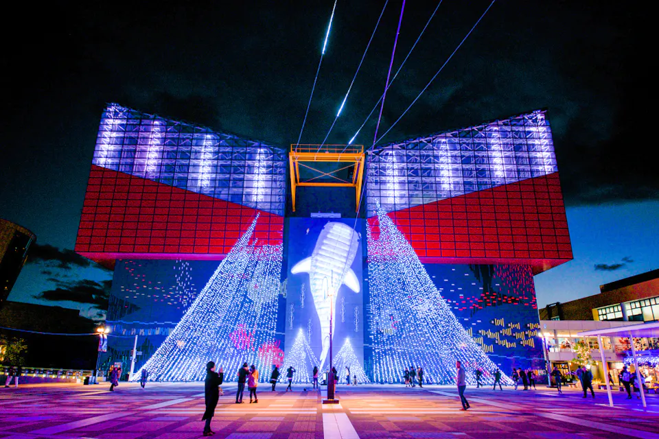 Osaka Aquarium Kaiyukan is located at Tempozan Harbor Village, Osaka, Japan A vibrant nighttime scene at an aquarium with a large, illuminated whale sculpture on display. The structure is adorned with blue and purple lights, creating a mesmerizing effect as visitors walk around the brightly lit plaza.