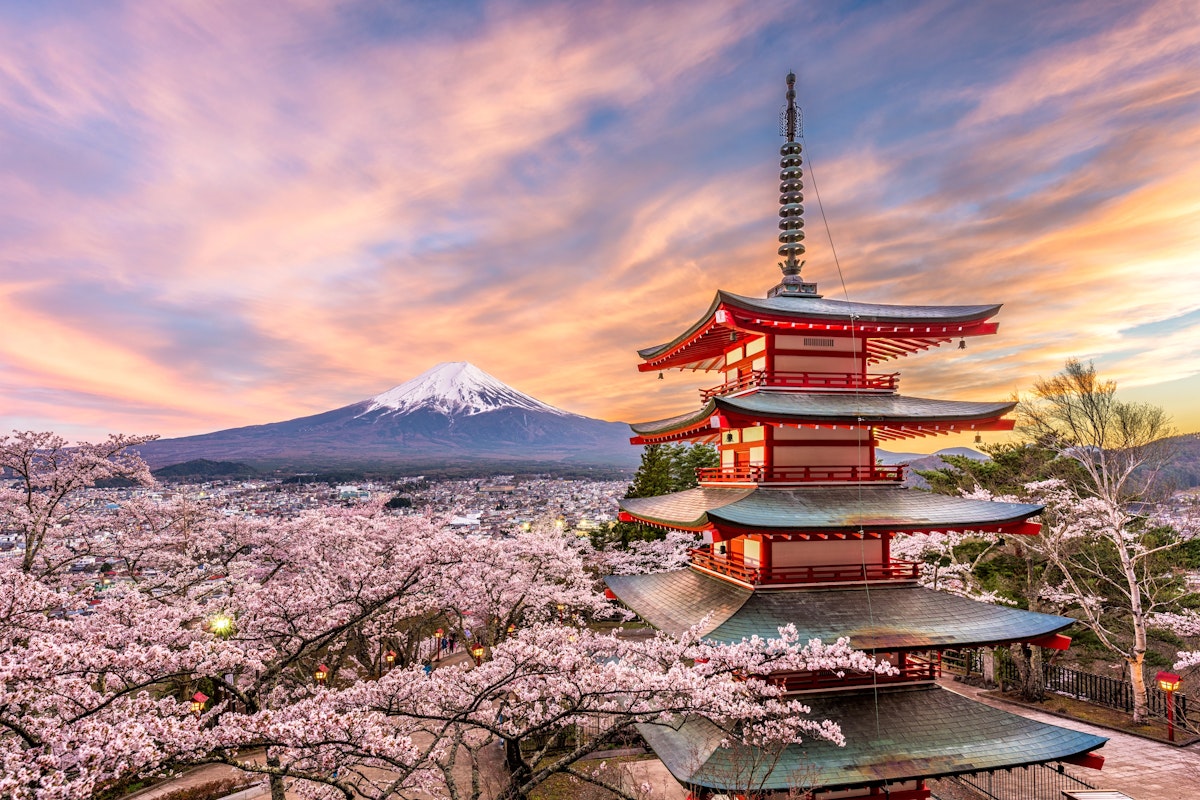 Mt. Fuji from Tokyo A five-story pagoda stands amid cherry blossoms, with Mount Fuji in the background under a vibrant sunset sky. The scene captures the serene beauty of the Japanese landscape in spring.