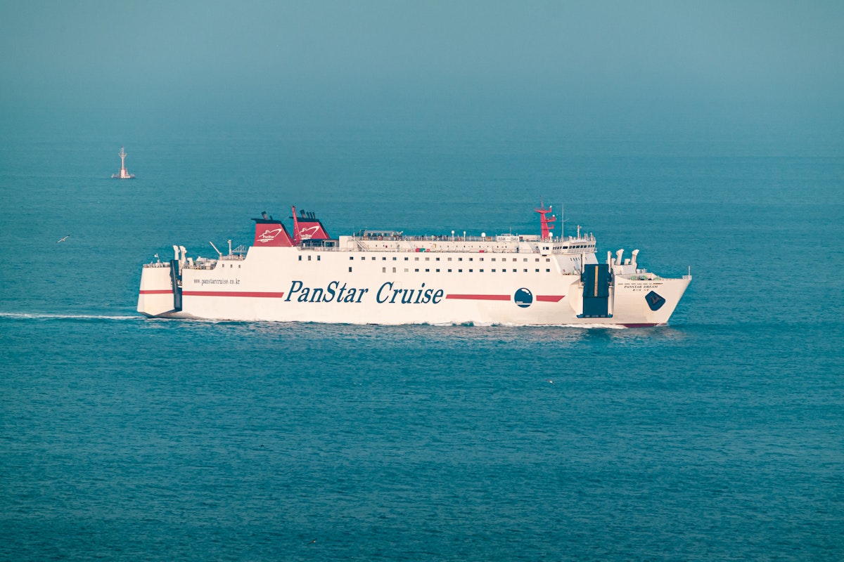 Traveling from Busan to Osaka A white ferry labeled "PanStar Cruise" moves across calm, blue waters under a clear sky. The ship's red and black details contrast with the sea, and a distant buoy is visible in the background.
