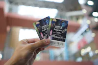 A hand holds two Osaka Amazing Pass 2-day tickets against a blurred background of what appears to be an indoor setting. The tickets feature cityscape imagery with a ferris wheel and other attractions.