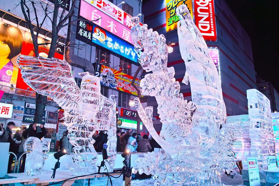Why January Is a Great Time to Visit Japan Intricate ice sculptures displayed on a city street at night. The sculptures are illuminated, showcasing detailed designs, while colorful signs and buildings are visible in the background, creating a vibrant urban atmosphere.