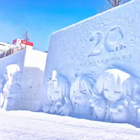 Experience Winter Festivals Snow sculptures depicting various anime characters are showcased at a winter festival. One sculpture features "20th Anniversary" engraved on it. Snow covers the ground and trees, while buildings are visible in the background under a clear blue sky.
