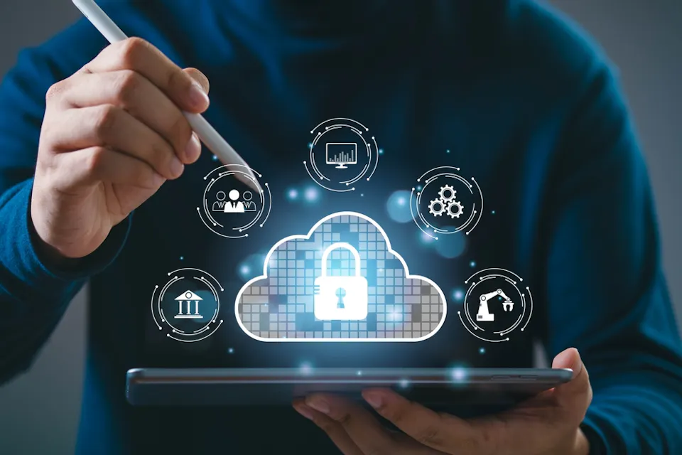 A person uses a stylus on a tablet. A digital cloud graphic with a lock symbol is displayed, surrounded by icons representing different technologies and data, such as graphs, gears, and a globe, indicating data security and cloud computing concepts.