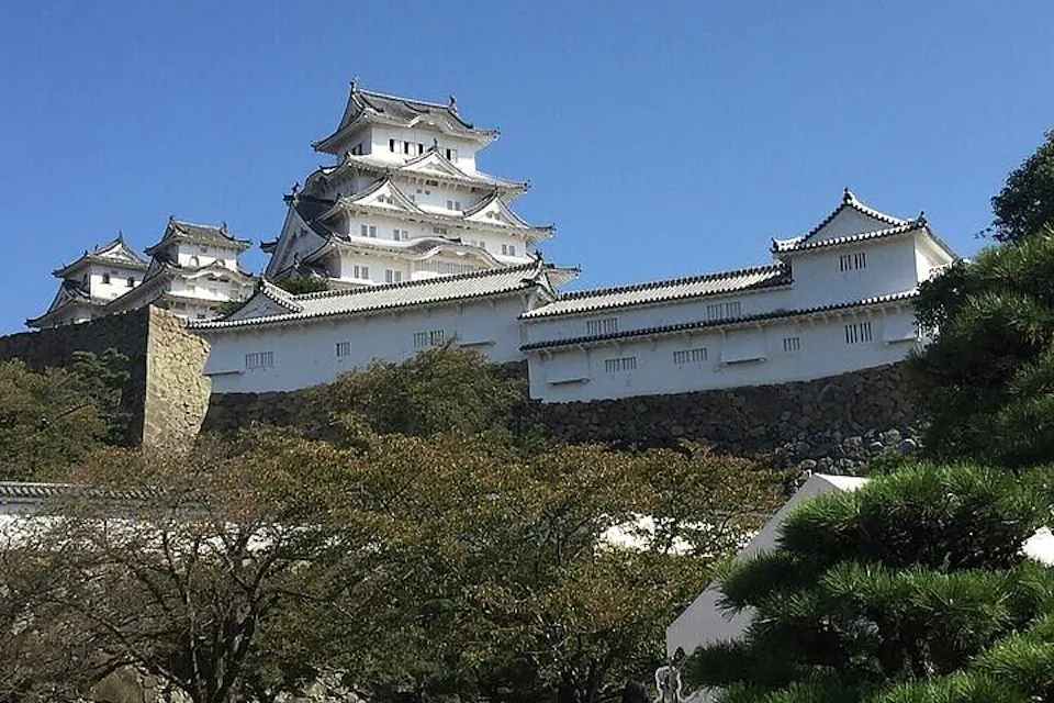 Himeji Castle's white main keep and fortified walls rising above stone ramparts under a clear blue sky in Hyogo, Japan.
