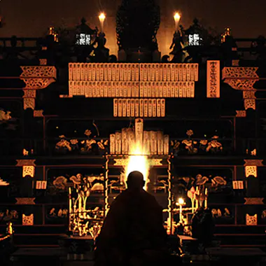 Tokyo Highlights Tour A person sits in front of an ornate altar illuminated by candlelight, with golden decorations, intricate carvings, and tablets, creating a warm, spiritual atmosphere.