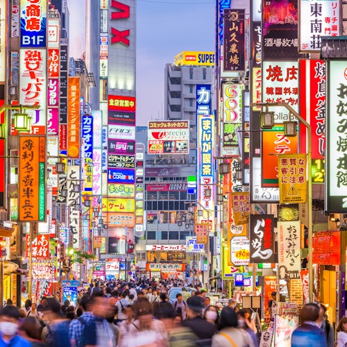 Tokyo for Modern Japanese Fusion A bustling street in Tokyo, Japan, filled with people and vibrant illuminated signs in various colors. The signs are in Japanese, featuring ads for shops, restaurants, and entertainment. The vibrant atmosphere suggests a lively urban area.
