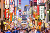 A bustling street in Tokyo, Japan, filled with people and vibrant illuminated signs in various colors. The signs are in Japanese, featuring ads for shops, restaurants, and entertainment. The vibrant atmosphere suggests a lively urban area.