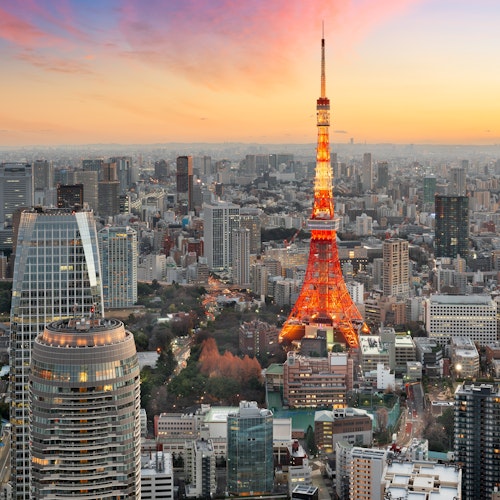 Things to Do in Tokyo Aerial view of Tokyo at sunset, featuring Tokyo Tower illuminated in orange. Surrounding skyscrapers and cityscape are bathed in warm, glowing hues, with a mix of modern architecture and lush greenery. A pink and orange sky adds to the scene's vibrancy.