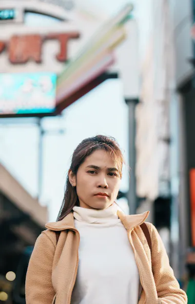 Ameyoko A woman in a tan coat and white turtleneck stands in a busy outdoor street market with Japanese signs and a vending machine visible in the background.