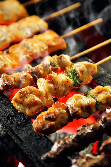 Skewers of grilled meat and vegetables cook over a charcoal grill, with visible smoke and red-hot embers below, creating a delicious, smoky atmosphere.
