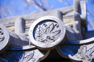 Close-up of traditional Japanese roof tiles with an ornate butterfly design carved into the circular end pieces, set against a clear blue sky.