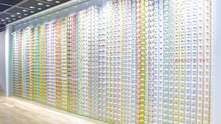 A brightly lit wall displays hundreds of colorful instant noodle cups arranged in neat vertical rows inside a modern building, creating a vibrant and organized pattern.