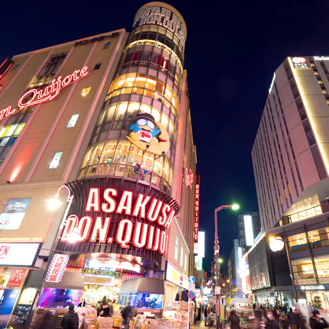 Don Quijote Asakusa A busy Tokyo street at night featuring the brightly lit Don Quijote store in Asakusa, with neon signs and tall buildings, as people walk along the sidewalks.
