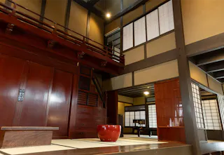 A traditional Japanese interior with tatami mats, sliding shoji doors, wooden cabinets, and a red lacquered bowl in the center, featuring warm wood tones and soft lighting.