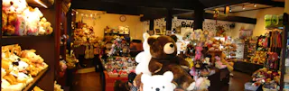 A cozy store filled with shelves and displays of various stuffed animals and plush toys, including large teddy bears. The warm lighting and organized layout create a welcoming atmosphere.