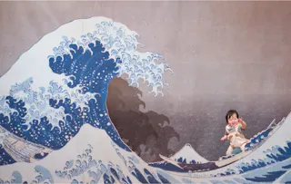 A smiling child poses in front of an art mural depicting the famous wave from Hokusai’s “The Great Wave off Kanagawa,” making it look like the child is part of the scene in the artwork.