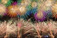 Colorful fireworks explode in the night sky, creating vibrant patterns of red, green, yellow, purple, and white above a dark landscape, illuminating the scene with bright, festive light.