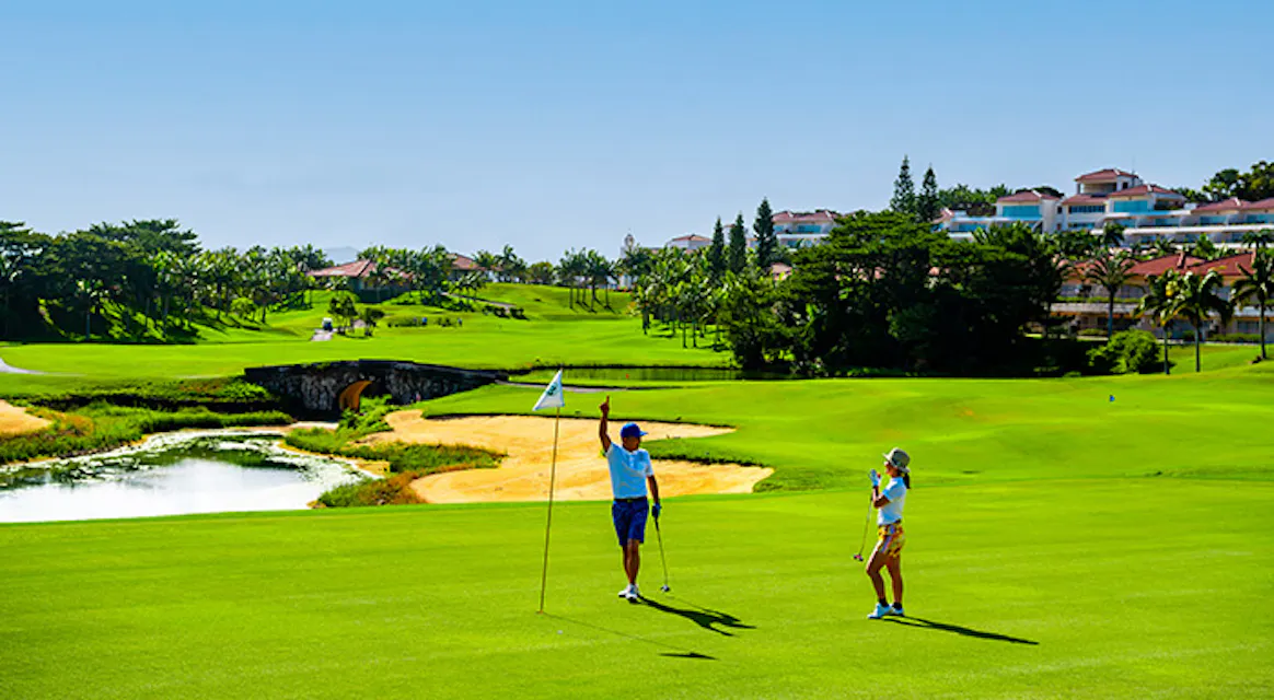 Two golfers celebrating on a green beside the flagstick at Kanucha Golf Course with a pond and bunkers behind