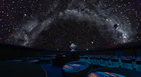 A dark planetarium with rows of empty seats and a star projector in the center, displaying a realistic, star-filled night sky with the Milky Way across the domed ceiling.