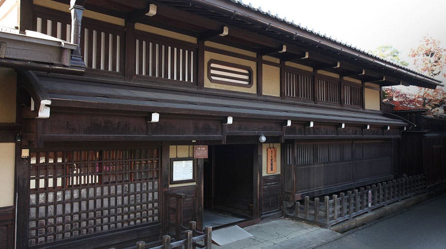 A traditional Japanese wooden building with sliding lattice doors, wooden railings, and a tiled roof, situated on a quiet street.