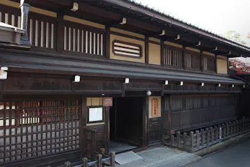 Kusakabe Folk Museum A traditional Japanese wooden building with sliding lattice doors, wooden railings, and a tiled roof, situated on a quiet street.
